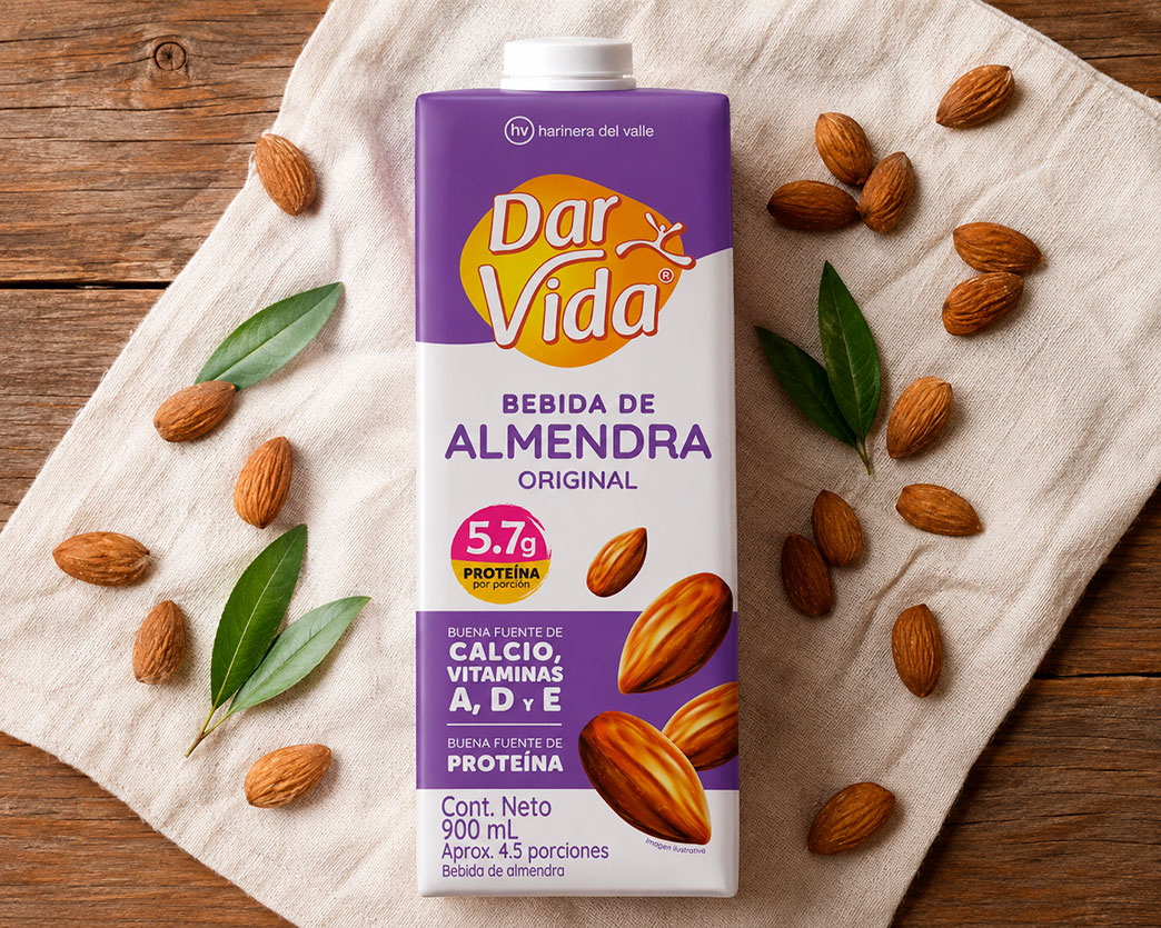 Empaque de Bebida de Almendra Original Dar Vida sobre una servilleta de tela beige en una mesa de madera, rodeado de almendras y hojas verdes decorativas.