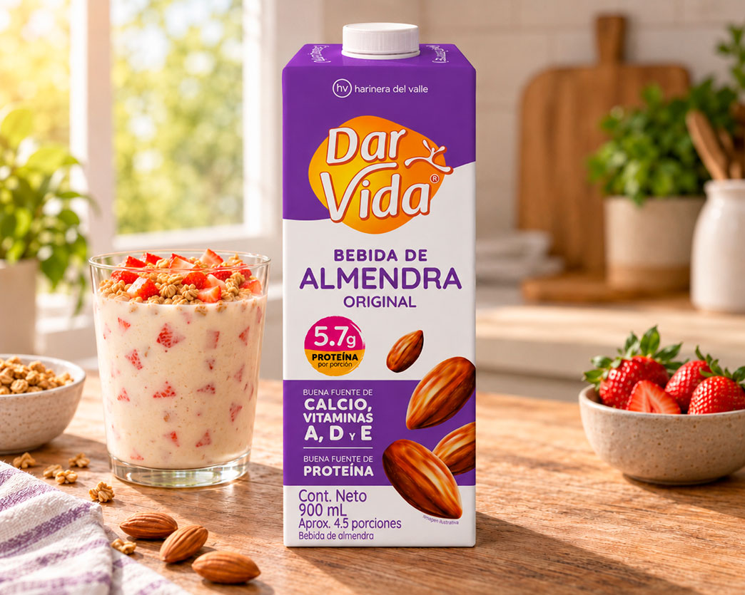 Empaque de Bebida de Almendra Original Dar Vida sobre una mesa de madera, acompañado de un vaso con bebida cremosa, fresas, granola y almendras. Al fondo se observa una cocina iluminada con luz natural, plantas y elementos de madera.